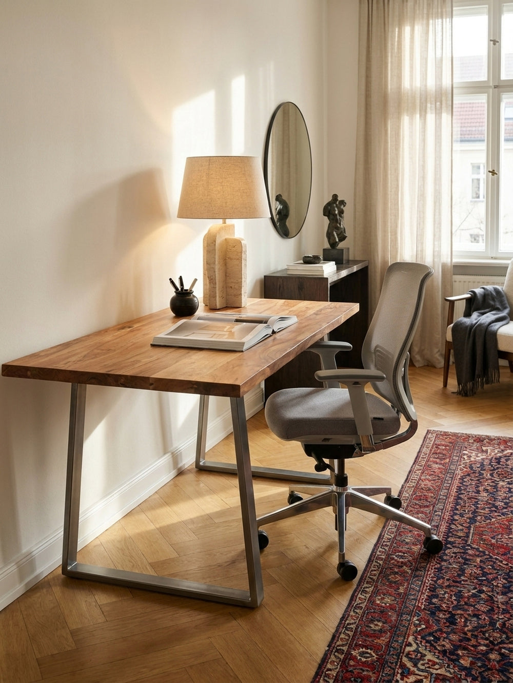 Der Bürotisch aus Massivholz kombiniert mit einem schwarzen Design-Bürostuhl und einem schwebenden Wandregal vor einer Kalkputzwand._