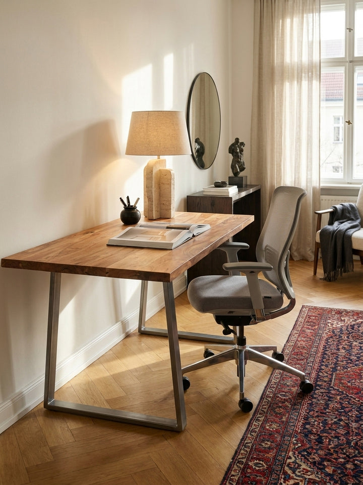 Der Bürotisch aus Massivholz kombiniert mit einem schwarzen Design-Bürostuhl und einem schwebenden Wandregal vor einer Kalkputzwand._