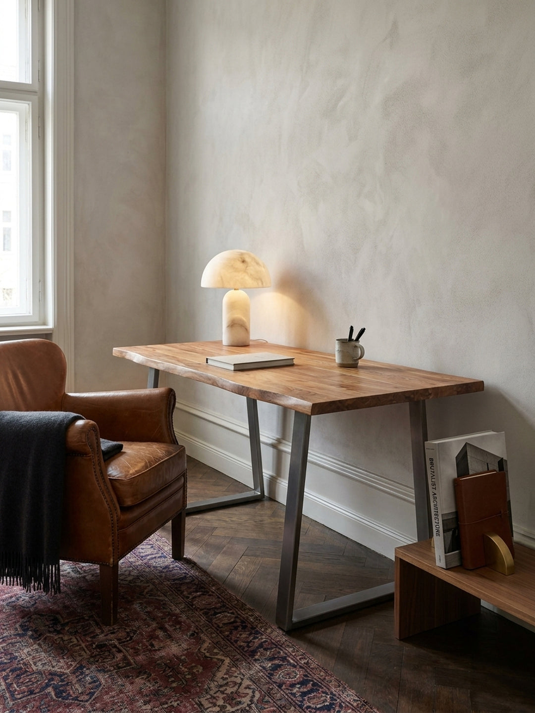 Der Massivholz-Schreibtisch 120x60 cm kombiniert mit einem ergonomischen Bürostuhl aus schwarzem Leder und einem niedrigen Bücherregal für ein stimmiges Arbeitszimmer-Design._