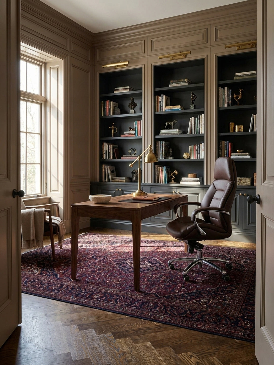 Ein brauner Bürostuhl aus Echtleder steht als zentraler Chefsessel hinter einem dunklen Nussbaumschreibtisch in einem luxuriösen Home Office mit Fischgrätparkett._