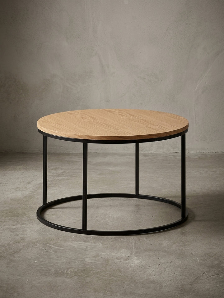 Moderner runder Couchtisch (70 cm Durchmesser) mit Eichenfurnier-Tischplatte und schwarzem Stahlgestell, freigestellt vor weißem Hintergrund aus frontaler Ansicht._