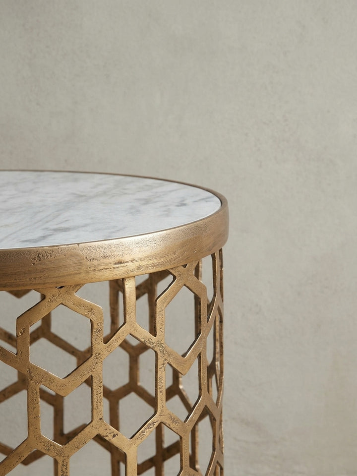 Nahaufnahme der Kante, wo die 1,5 cm starke, weiße Marmorplatte präzise in den goldenen Metallrahmen des modernen Beistelltischs für das Wohnzimmer eingelassen ist._