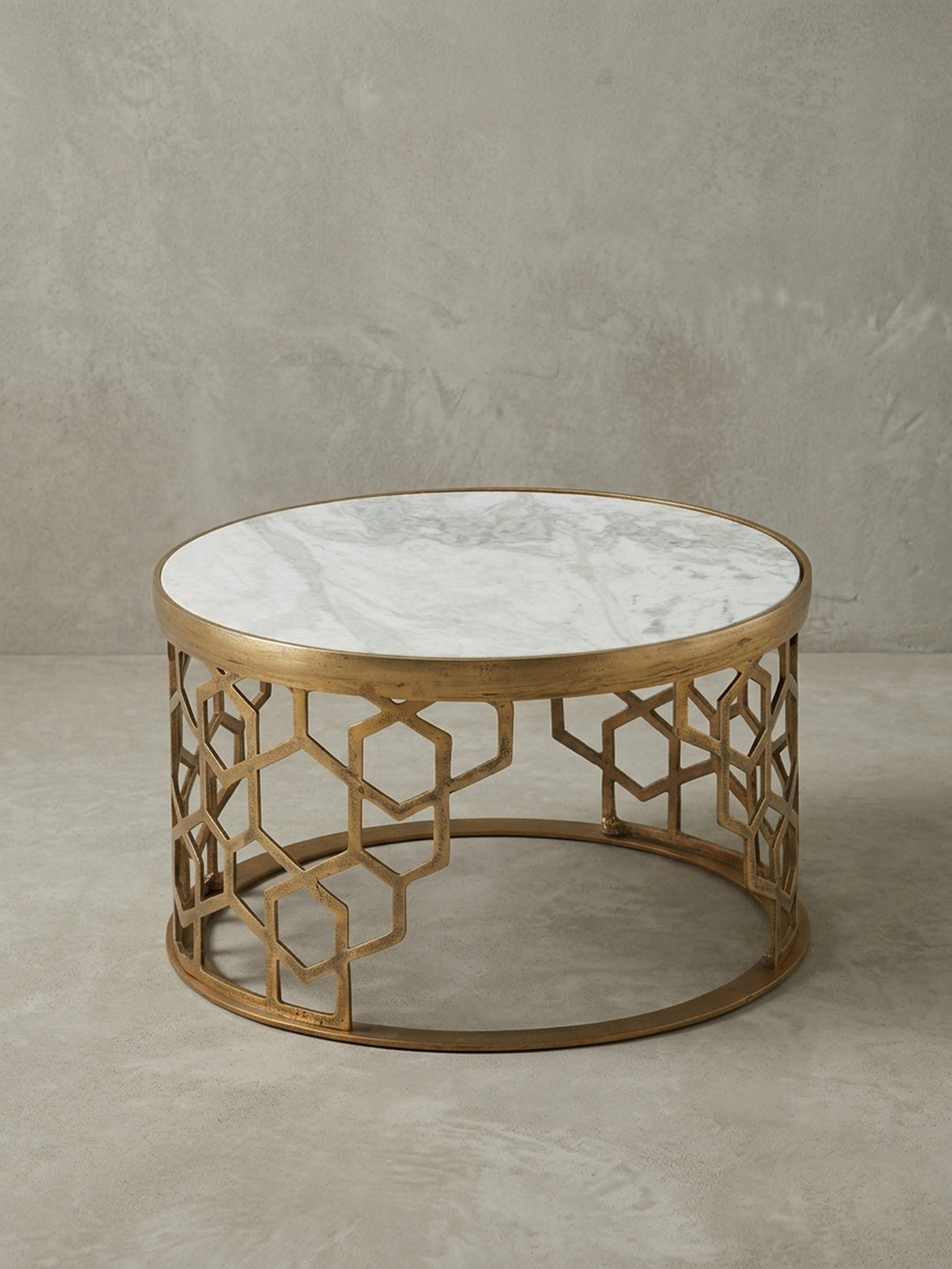 Der runde Marmor-Couchtisch aus einer alternativen Perspektive, die das Lichtspiel auf der polierten Marmoroberfläche und dem satinierten Gold-Finish des Gestells einfängt._