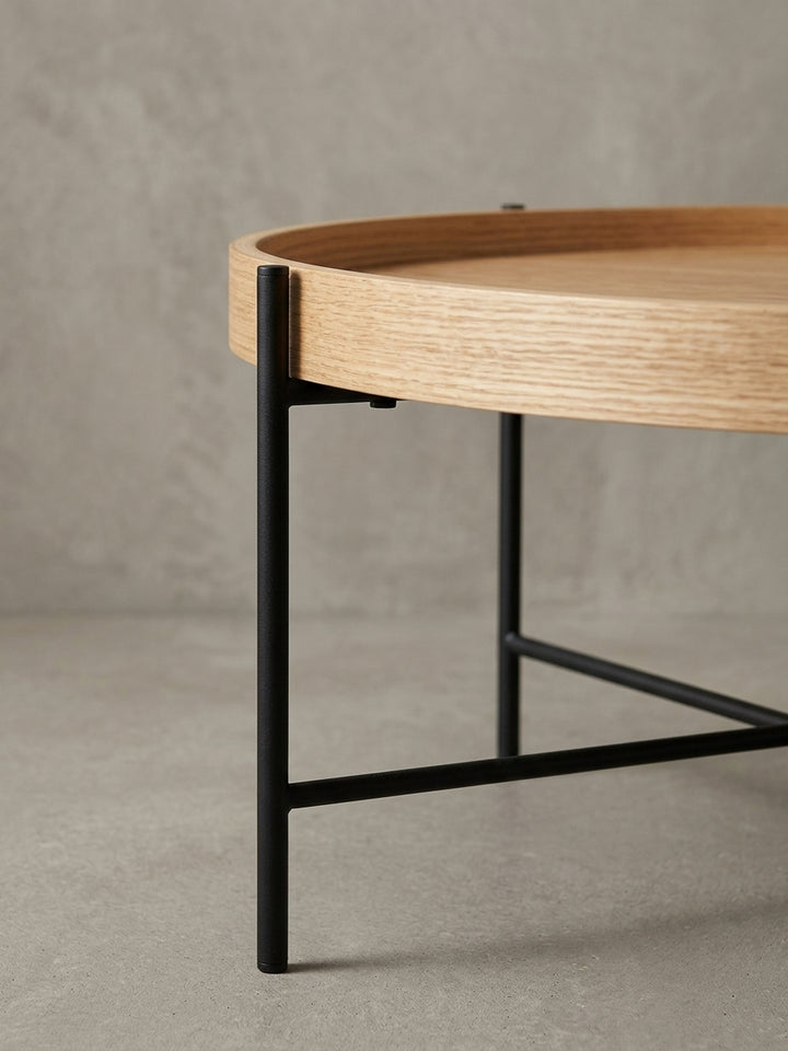 Nahaufnahme eines Details des Couchtischs: die saubere Verbindung zwischen dem schwarzen Metallbein und der Unterseite der runden Tischplatte aus Eichenholz._