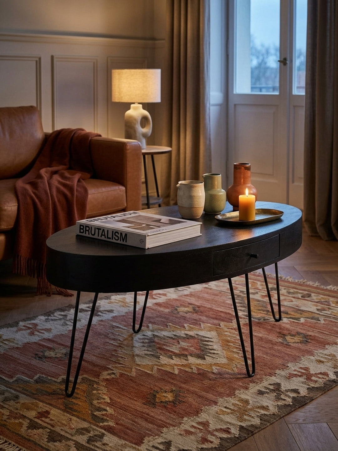 Auf dem schwarzen Sofatisch mit Haarnadelbeinen liegt ein Kunstbuch neben einer Keramikvase, was eine gemütliche Wohnatmosphäre schafft._