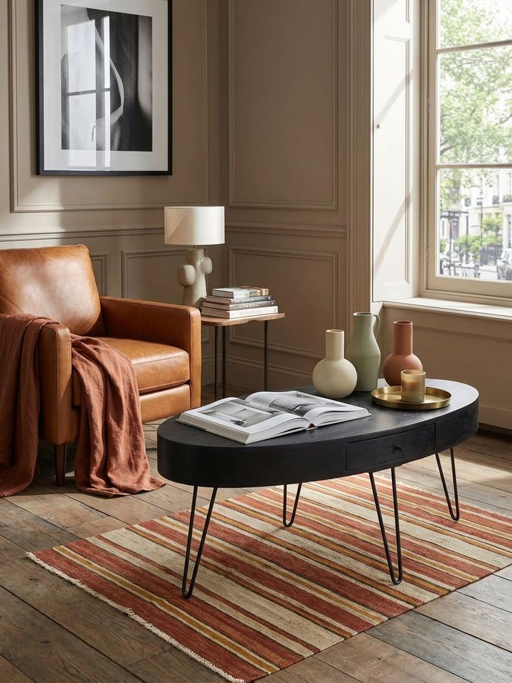 Der ovale Kaffeetisch aus Holz und Metall als perfekter Begleiter zu einem modernen Ledersessel und einem hellen Bouclé-Sofa im Wohnzimmer._