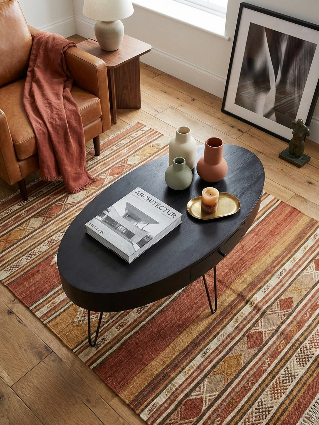 Design-Wohnzimmertisch in Ovalform von oben betrachtet, zeigt die großzügige Ablagefläche aus Massivholz und die Anordnung auf einem gemusterten Teppich._