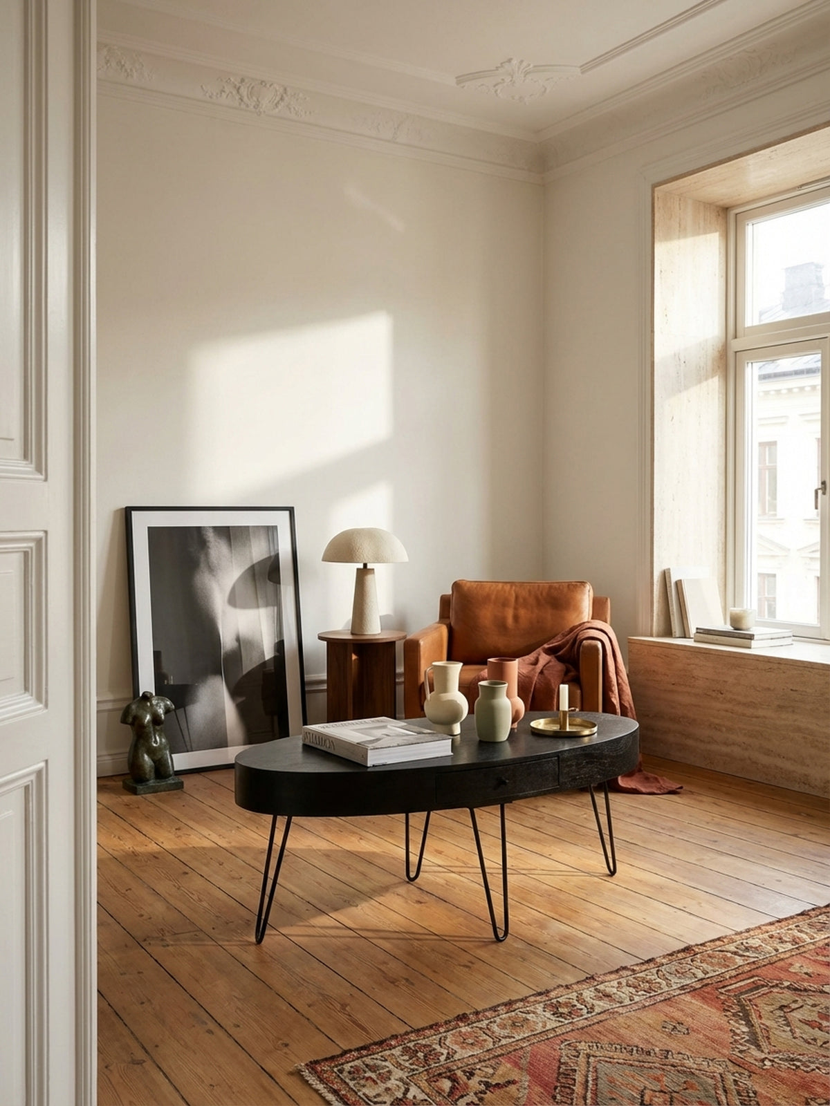 Eleganter ovaler Couchtisch aus schwarzem Mangoholz im Mittelpunkt eines lichtdurchfluteten Wohnzimmers mit beigem Sofa und Vintage-Kilim-Teppich.