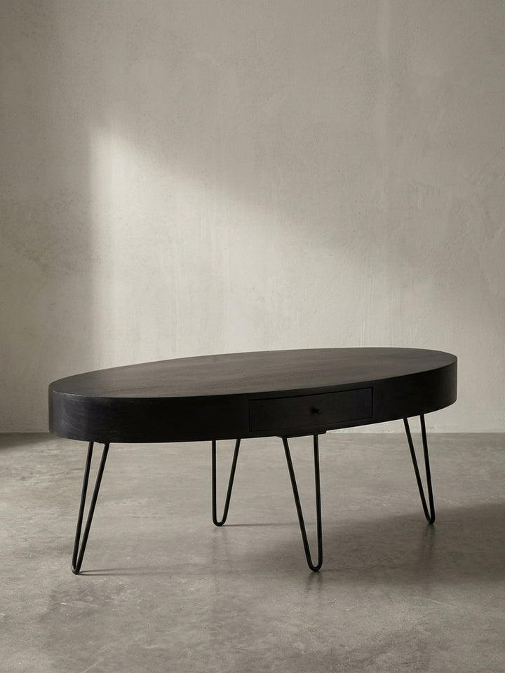 Frontansicht des ovalen Couchtisches aus massivem Mangoholz in Schwarz, der seine klare Silhouette und die filigranen Haarnadelbeine zeigt._