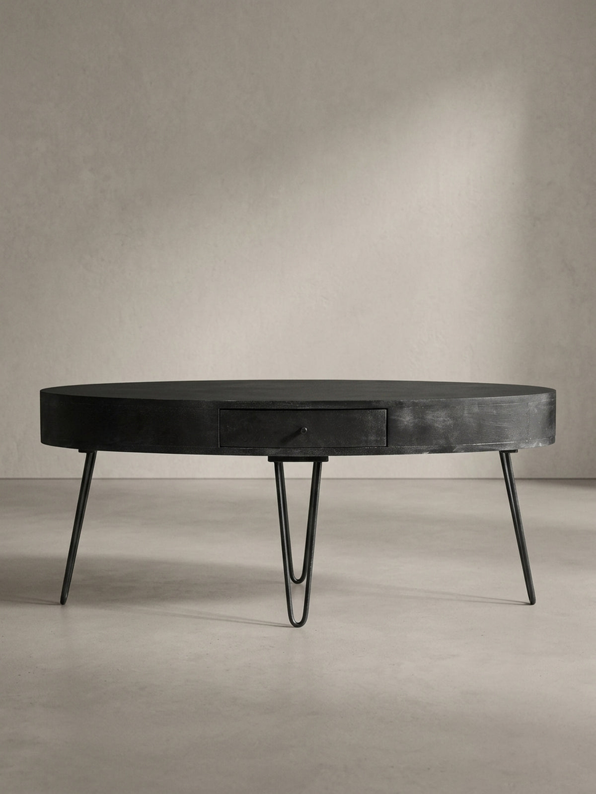 Der schwarze Design-Couchtisch in 3/4-Ansicht, die die unauffällig integrierte Schublade und die Stabilität der sechs Metallbeine betont.