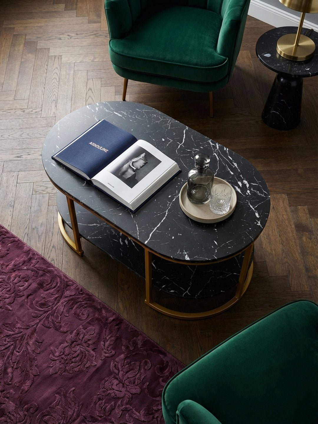 Blick von oben auf den Design-Couchtisch mit zwei Ablagen, arrangiert auf einem seidenen Pflaumen-Teppich neben einem smaragdgrünen Samtsofa in einem stilvollen Altbau._