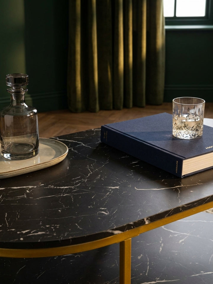 Nahaufnahme der Tischplatte in täuschend echter schwarzer Marmor-Optik, die feine weiße Maserung des modernen Kaffeetisches reflektiert das sanfte Licht einer Lampe._
