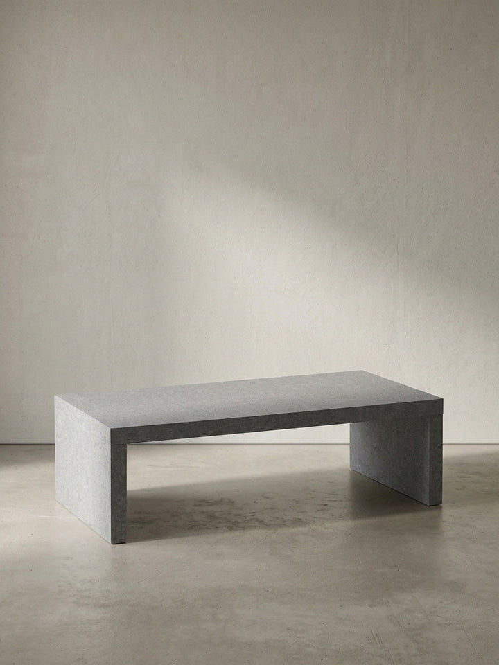 Grauer Couchtisch in klarer Beton-Optik mit den kompakten Maßen 110x55x35 cm frontal vor einem neutralen, reinweißen Hintergrund_