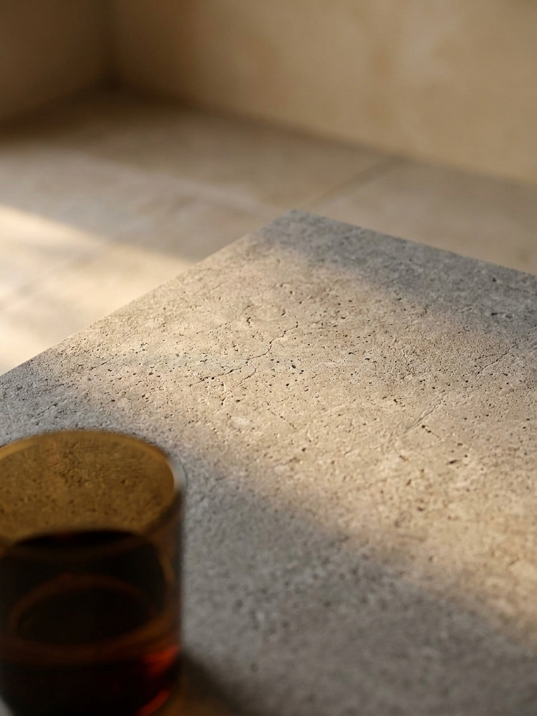 Nahaufnahme der matten Oberfläche des grauen Wohnzimmertisches in Beton-Optik, die die subtile architektonische Textur im warmen Licht detailliert zeigt_