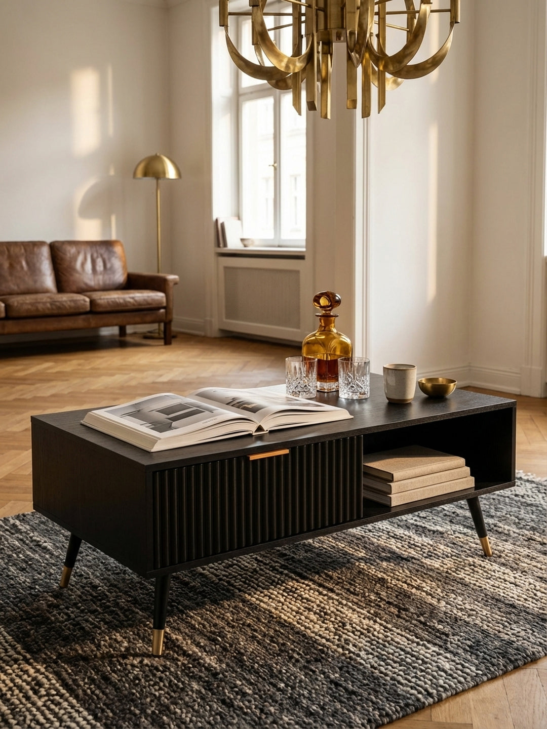Ein Stapel Architekturbücher und eine Whiskey-Karaffe arrangiert auf dem schwarzen Couchtisch, der eine gemütliche und intellektuelle Atmosphäre schafft._