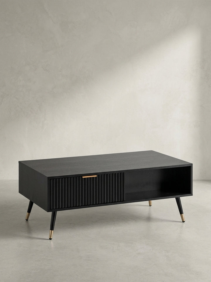 Seitenansicht des Kaffeetisches, die das schlanke Profil und die eleganten, schräg gestellten Metallbeine mit den goldenen Spitzen hervorhebt._