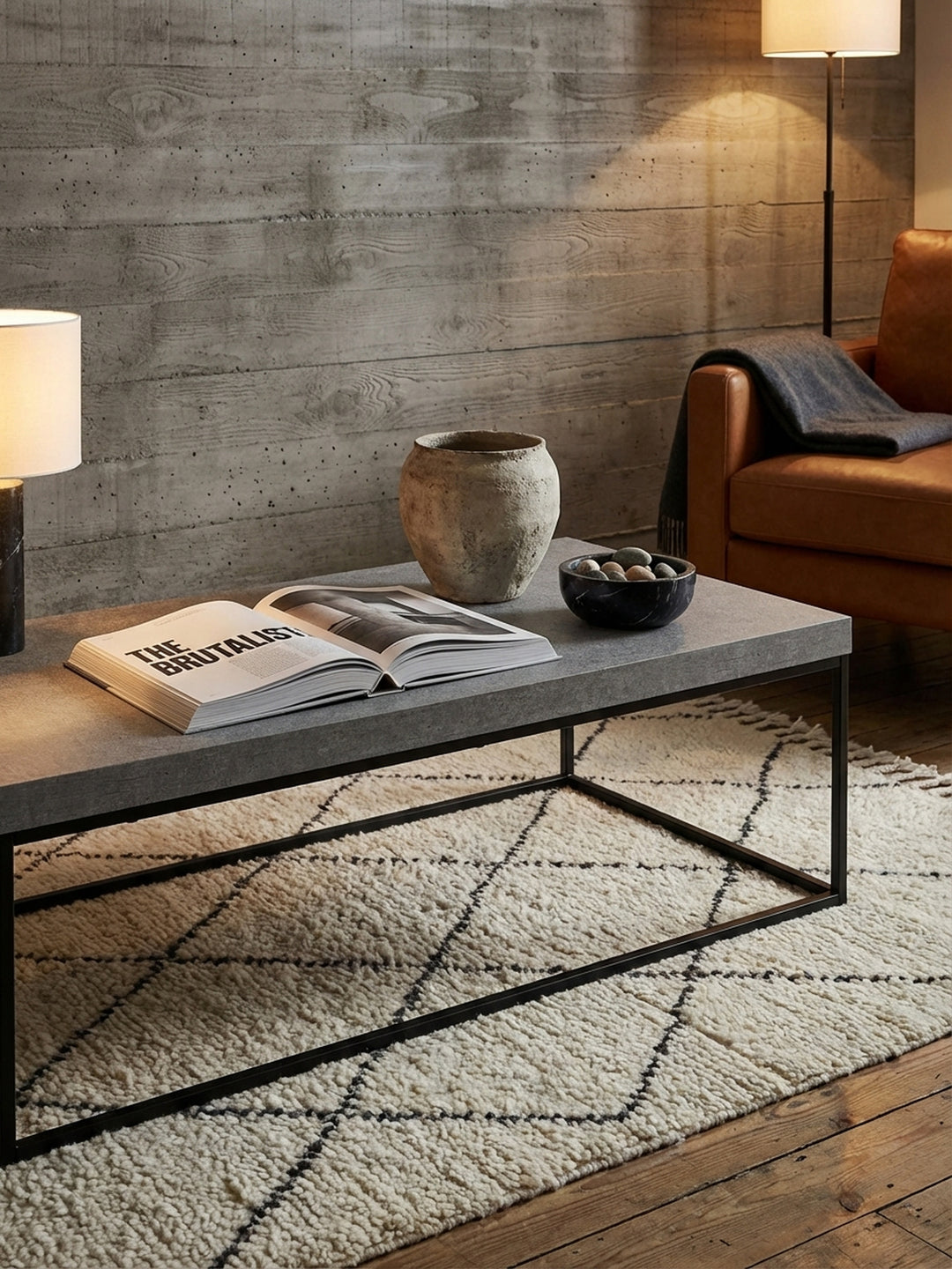 Styling-Detail auf einem modernen Couchtisch: ein Architekturbuch und eine handgefertigte Keramikvase auf der grauen Tischplatte._
