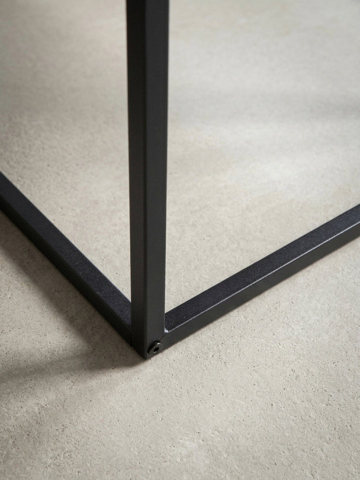 Detailaufnahme der präzisen Kante der 5 cm starken Tischplatte in Beton-Optik und der sauberen Verarbeitung des schwarzen Metallrahmens._