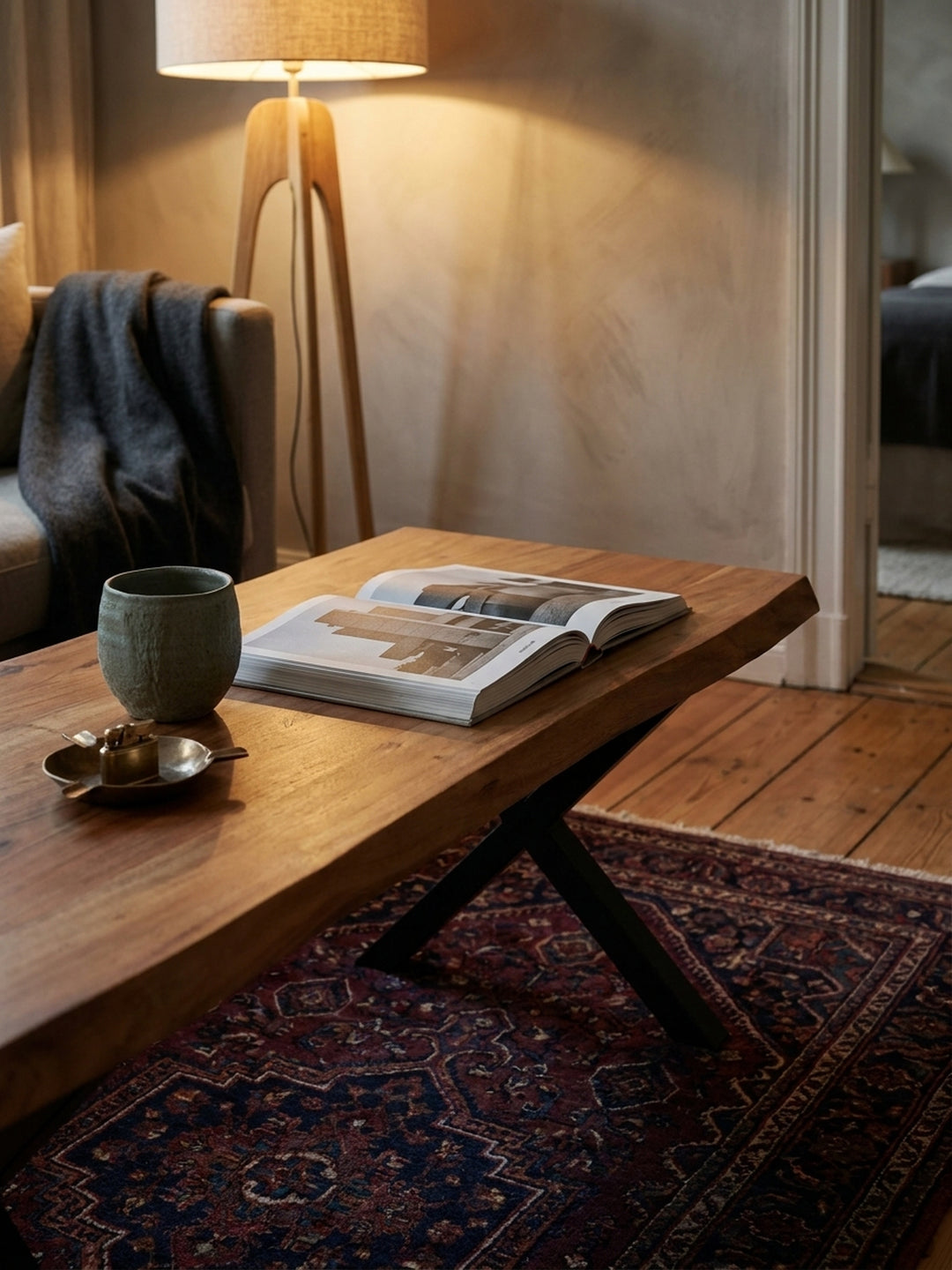 Ein aufgeschlagenes Buch und eine Keramikvase auf dem braunen Massivholztisch, der eine gemütliche Atmosphäre vor dem Sofa erzeugt._