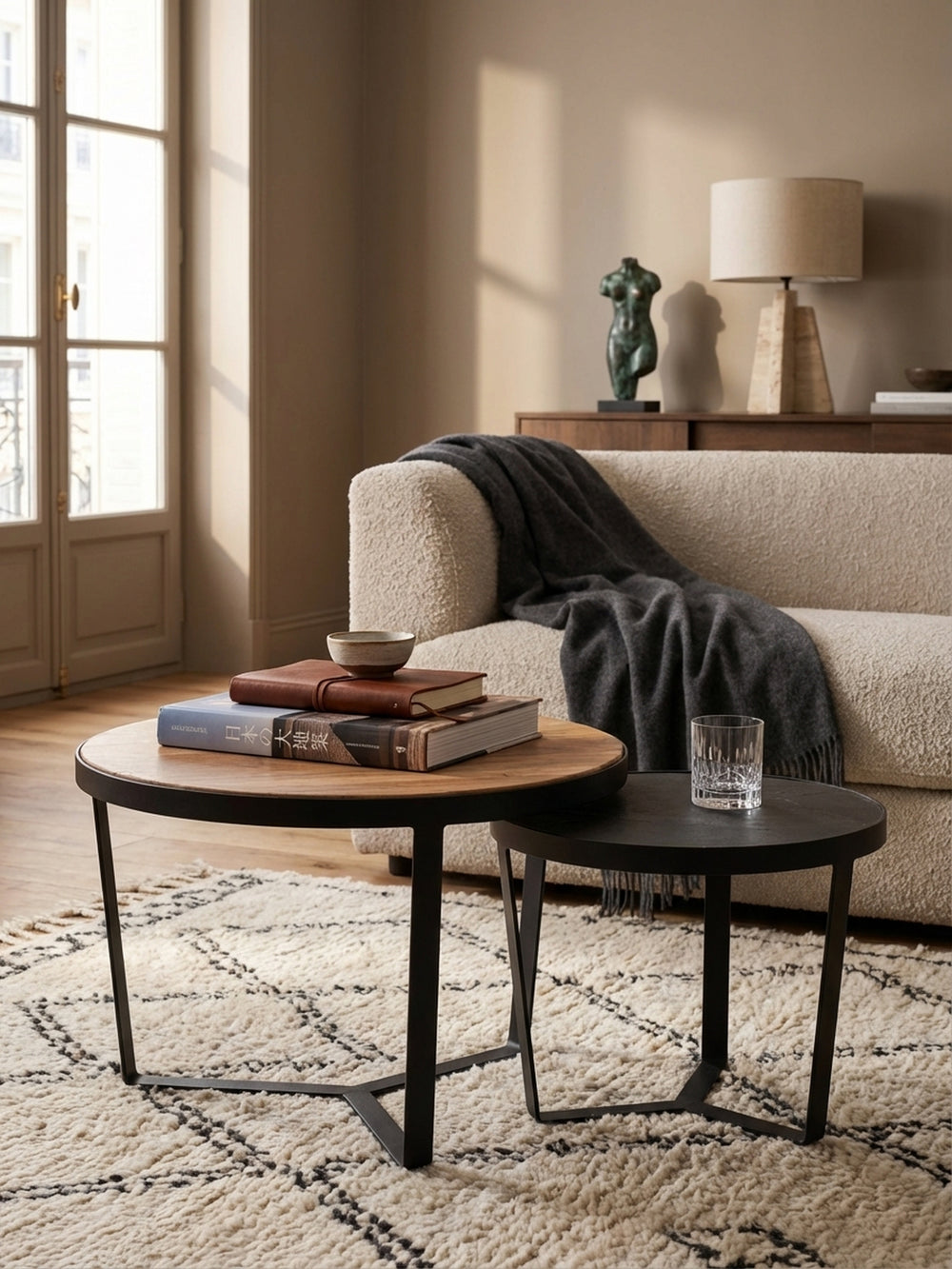 Moderner Couchtisch aus Akazie als Ablage für ein Kaffeetassen-Set und ein offenes Kunstbuch, daneben der kleinere Satztisch in Anthrazit._