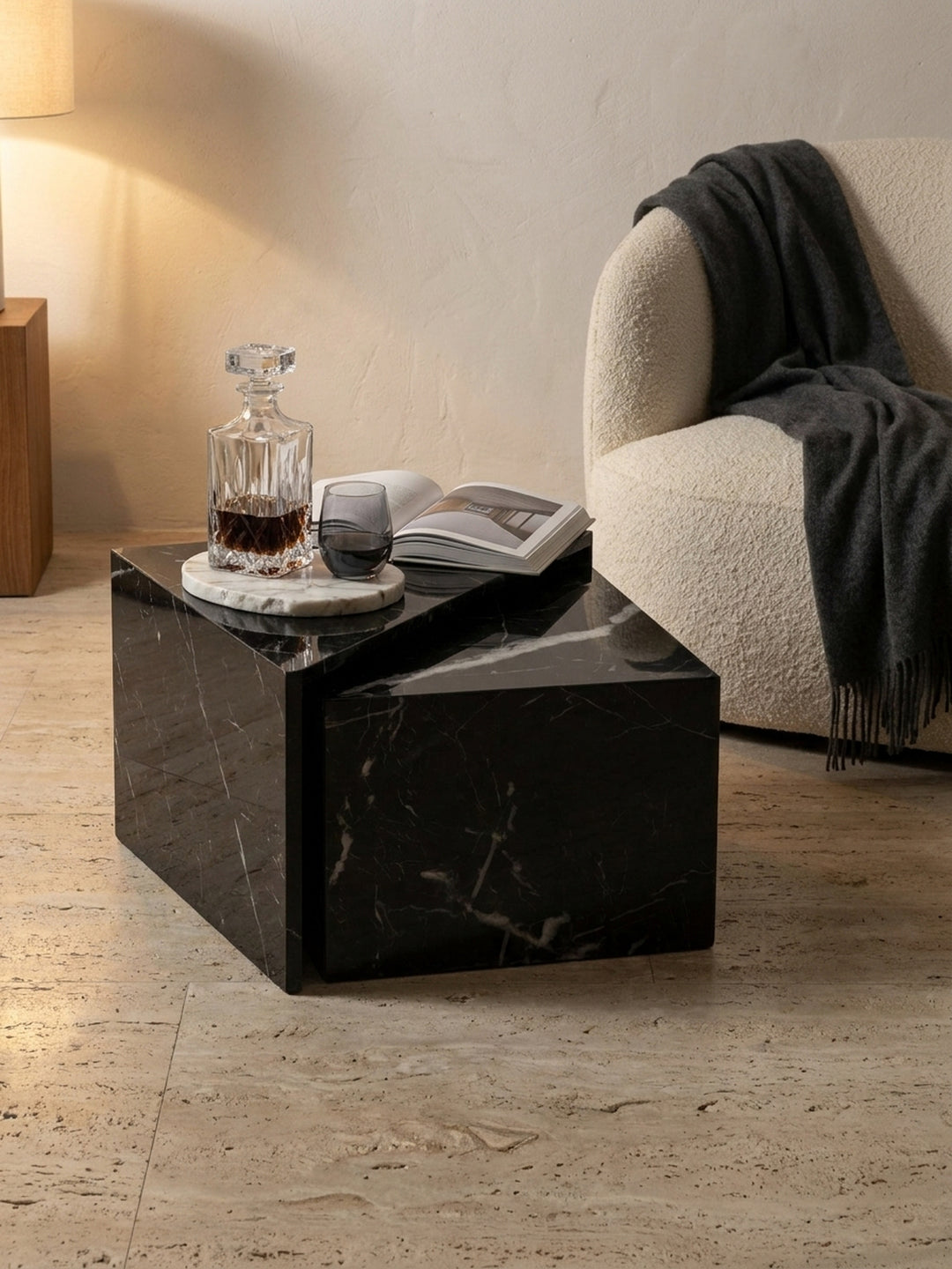 Kleiner Sofatisch in schwarzer Marmor-Optik, stilvoll arrangiert mit einer schweren Kristallkaraffe und einem dicken Bildband über Architektur neben einer dunklen Leselampe_