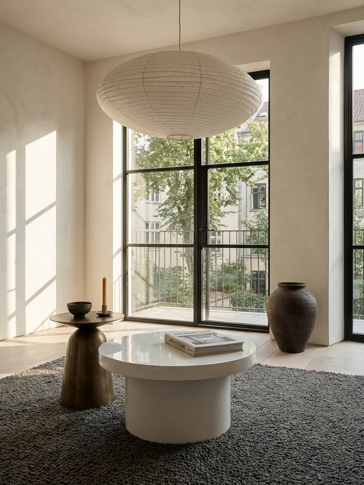 Der kompakte, weiße Kaffeetisch mit 60 cm Durchmesser steht elegant neben einem beigefarbenen Stoffsofa und harmoniert mit dem hellen Holzboden des Raumes._