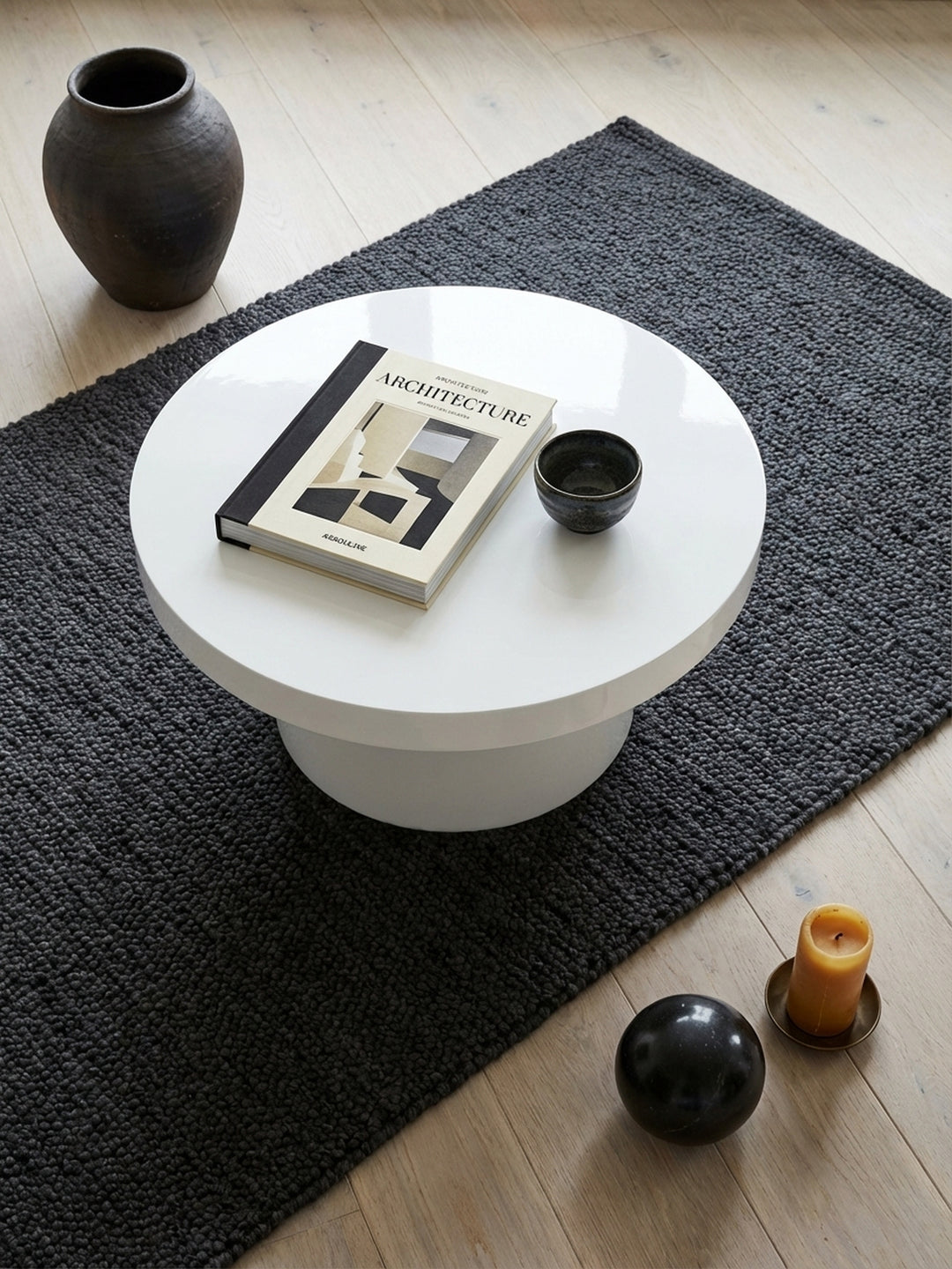 Runder Design-Sofatisch in Pilz-Form von oben betrachtet, zeigt die weiße Hochglanz-Oberfläche in Kombination mit einem grauen Sofa und einem Holzboden im Raum._