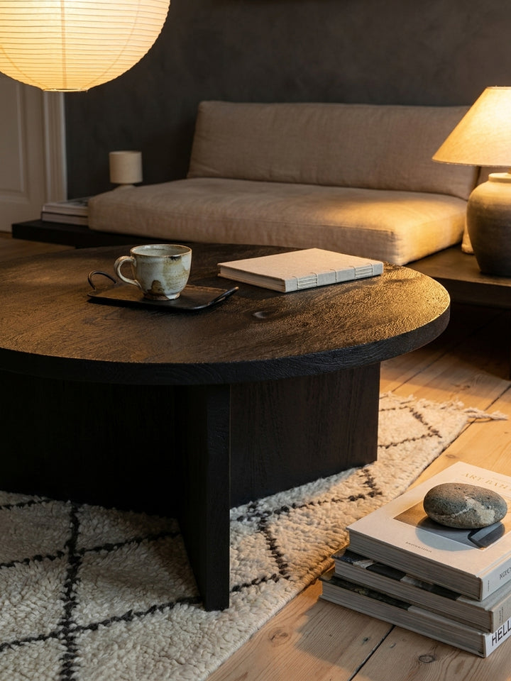 Stilvolles Arrangement auf dem runden, schwarzen Kaffeetisch: ein offenes Buch und ein Glas Wasser, das die schlichte Eleganz im Wohnzimmer unterstreicht._