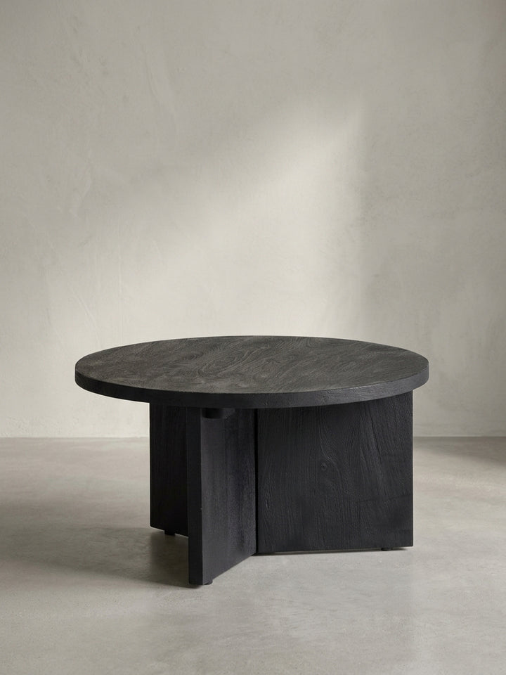 Frontansicht des runden Couchtisches aus schwarz sandgestrahltem Mangoholz, der sein minimalistisches Design und das stabile Dreibein-Gestell präsentiert._
