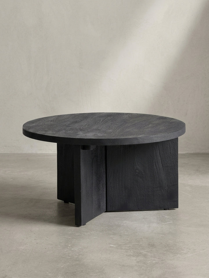 Schrägansicht des schwarzen Massivholz-Couchtisches, die die massive, runde Tischplatte und die geometrische Anordnung der drei Standbeine hervorhebt._