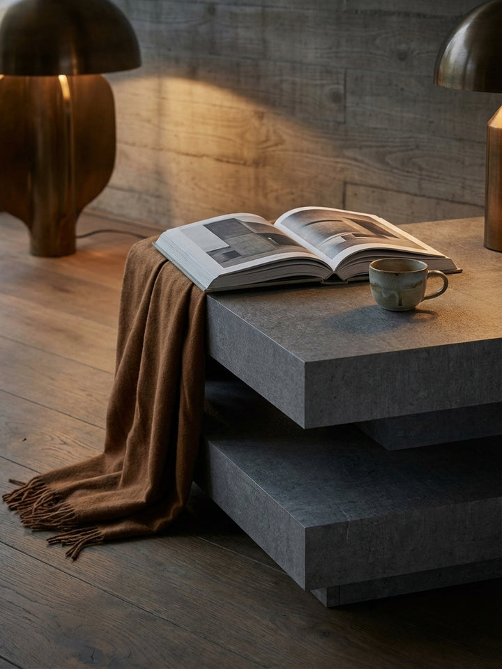 Ein Design-Magazin und eine rustikale Keramikvase mit Trockenblumen stilvoll auf dem modernen Betontisch im Wohnzimmer platziert._