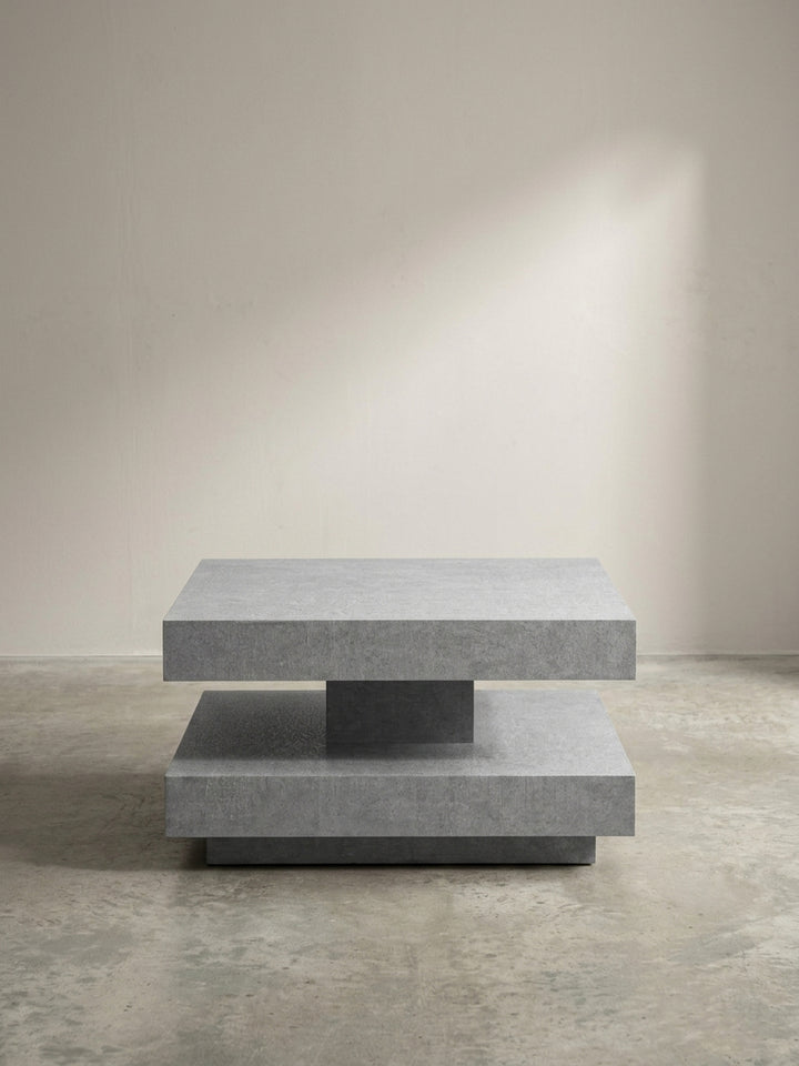 Schräge 3/4-Ansicht des modernen Sofatisches in Grau, die Tiefe und das geometrische Design der doppelten Ablagefläche betont._