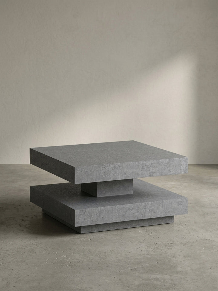 Frontansicht des quadratischen Couchtisches in Beton-Optik, der seine skulpturale, zweistufige Form auf weißem Hintergrund präsentiert._