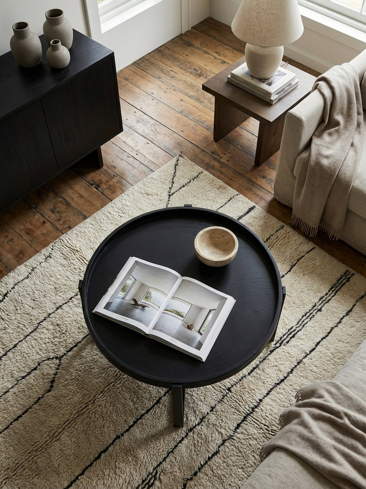 Draufsicht auf einen Industrial-Couchtisch mit Metallgestell, der auf einem texturierten Wollteppich vor einer modernen Couchgarnitur arrangiert ist._