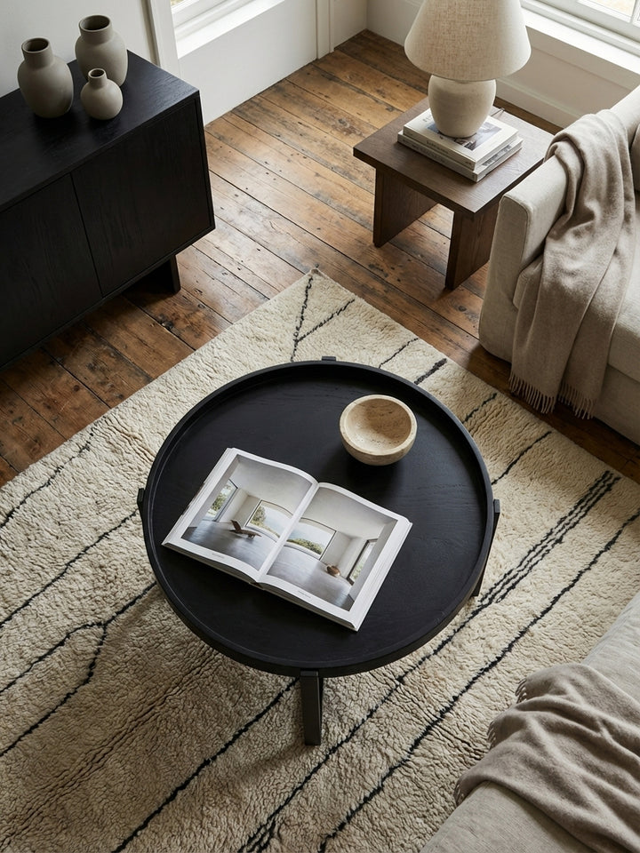 Draufsicht auf einen Industrial-Couchtisch mit Metallgestell, der auf einem texturierten Wollteppich vor einer modernen Couchgarnitur arrangiert ist._