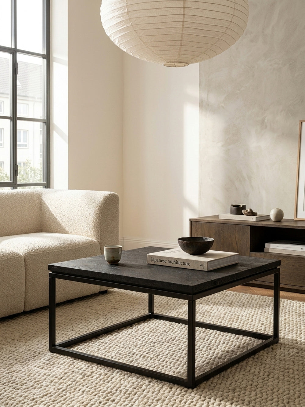 Schwarzer Kaffeetisch aus Mango Massivholz als stilvoller Begleiter zu einem tiefen Leinensofa und einem skulpturalen Sessel im minimalistischen Ambiente._