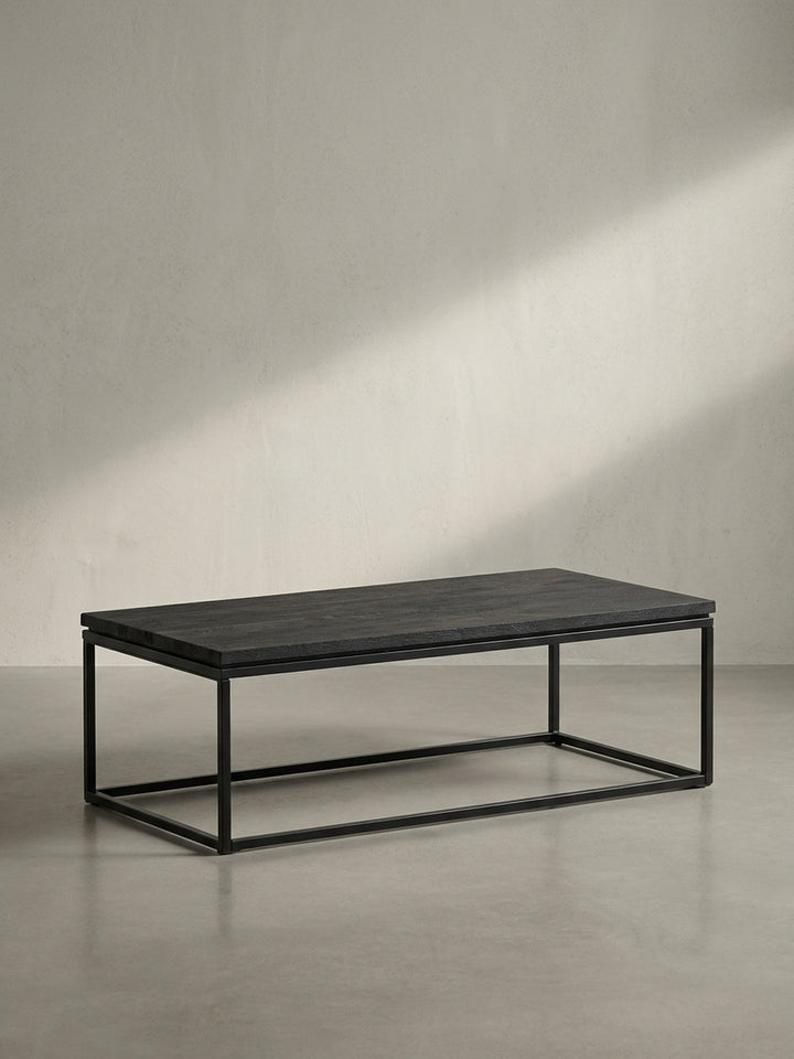 Frontansicht des minimalistischen Couchtisches mit 120x60 cm Tischplatte aus schwarzem Mangoholz und filigranem Metallgestell, freigestellt._