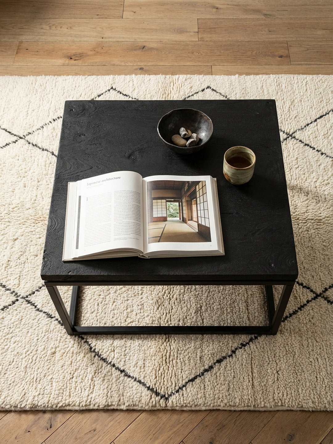 Moderner Sofatisch mit schwarzem Metallgestell und Massivholzplatte von oben betrachtet, arrangiert mit einem Architekturbuch und einer Keramikschale._