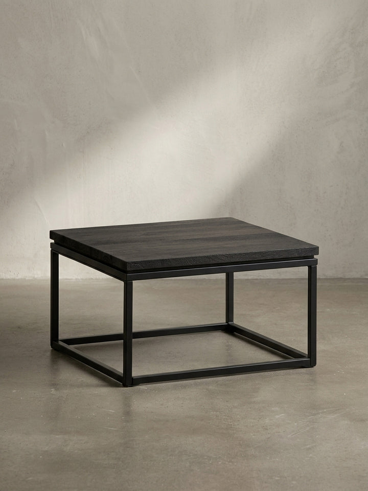 Design-Couchtisch aus schwarzem Holz und Metall in der Dreiviertelansicht, die die klare, kubische Form und die robuste Konstruktion hervorhebt._