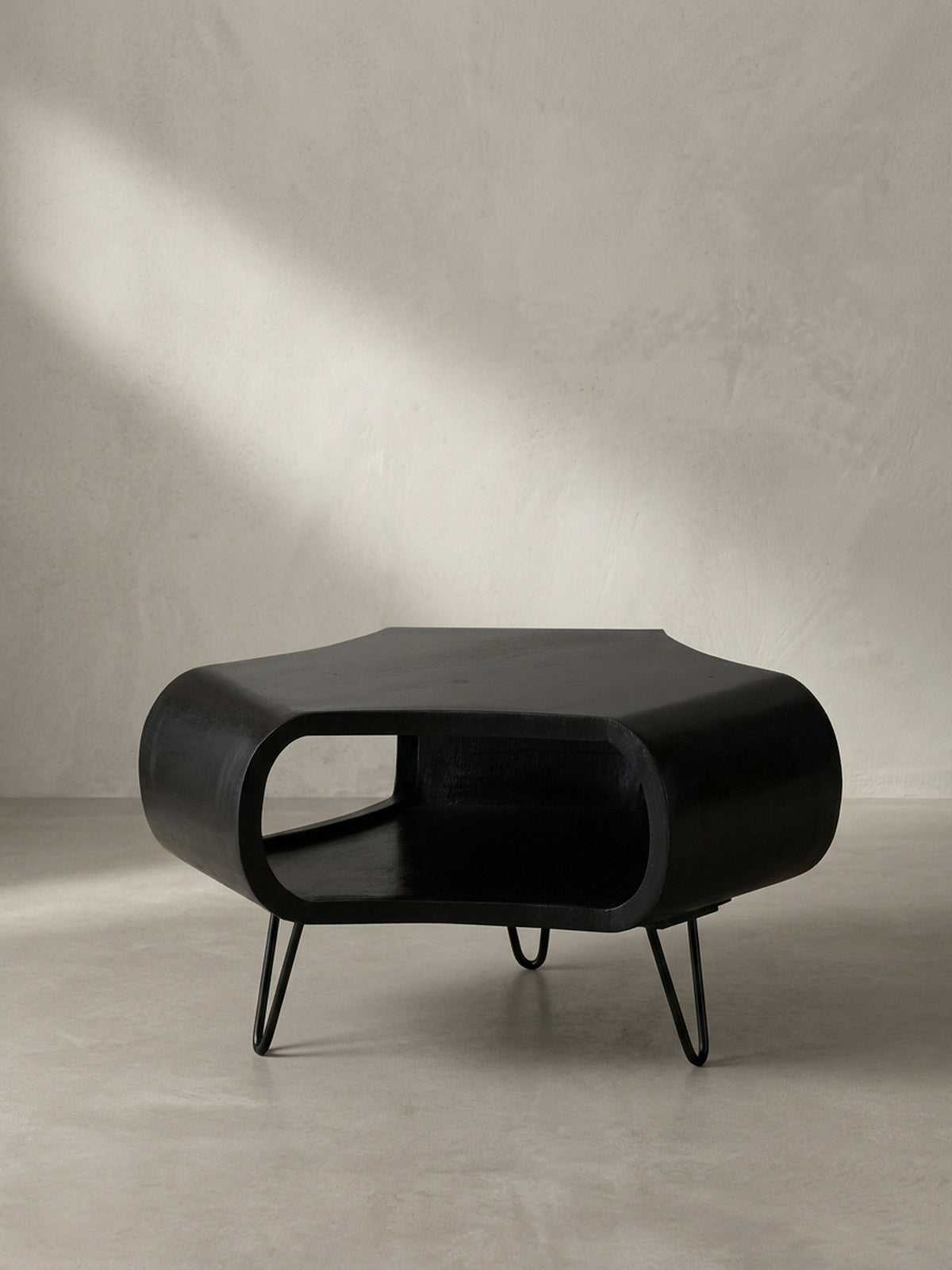 Gesamtansicht des handgefertigten Couchtisches aus schwarzem Mangoholz, dessen organische Form und massive Materialität ein einzigartiges Design-Statement für das Wohnzimmer setzt._