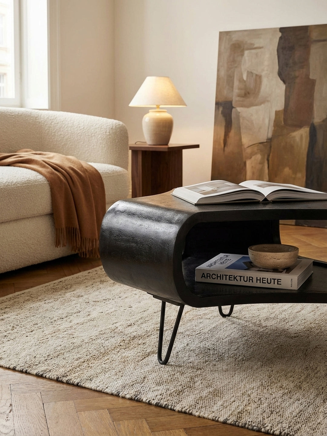 Ein schwarzer Sofatisch mit einem großen Bildband auf der Ablage, der eine gemütliche Leseecke neben einem modernen Sofa mit Leinenkissen im Wohnzimmer schafft._