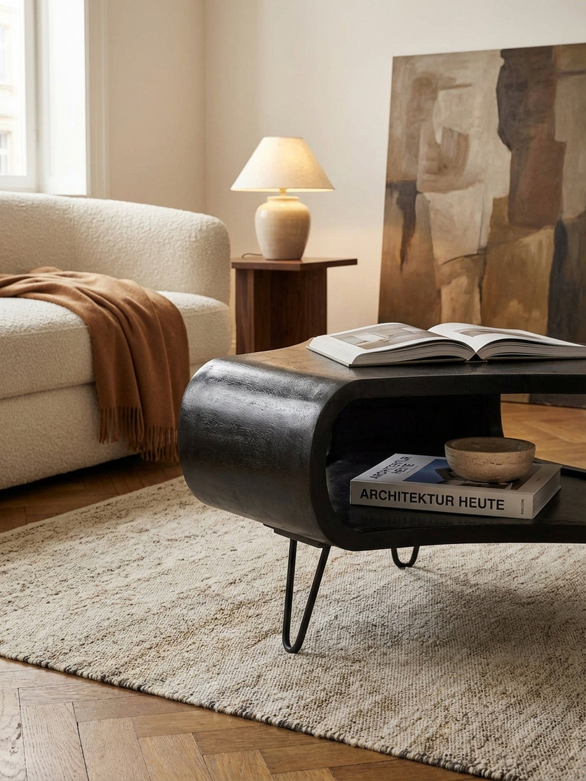 Ein schwarzer Sofatisch mit einem großen Bildband auf der Ablage, der eine gemütliche Leseecke neben einem modernen Sofa mit Leinenkissen im Wohnzimmer schafft.