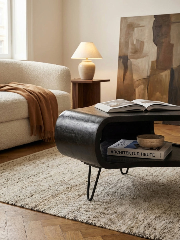 Ein schwarzer Sofatisch mit einem großen Bildband auf der Ablage, der eine gemütliche Leseecke neben einem modernen Sofa mit Leinenkissen im Wohnzimmer schafft._
