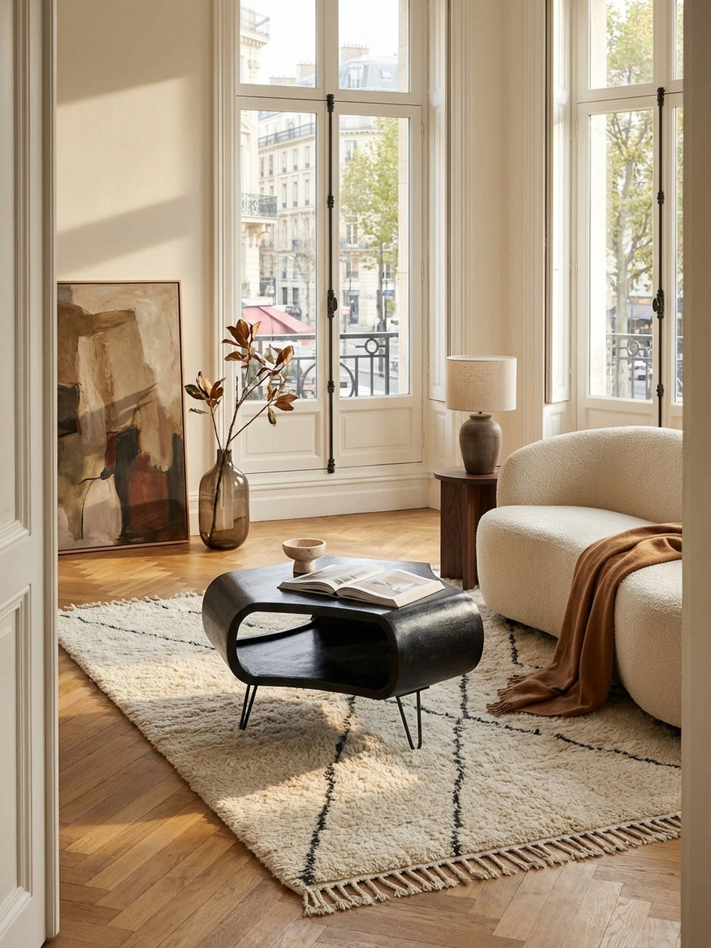 Skulpturaler schwarzer Couchtisch aus Mango-Massivholz auf einem hellen Beni Mrirt Teppich in einem eleganten Wohnzimmer mit Fischgrätparkett und bodentiefen Fenstern._