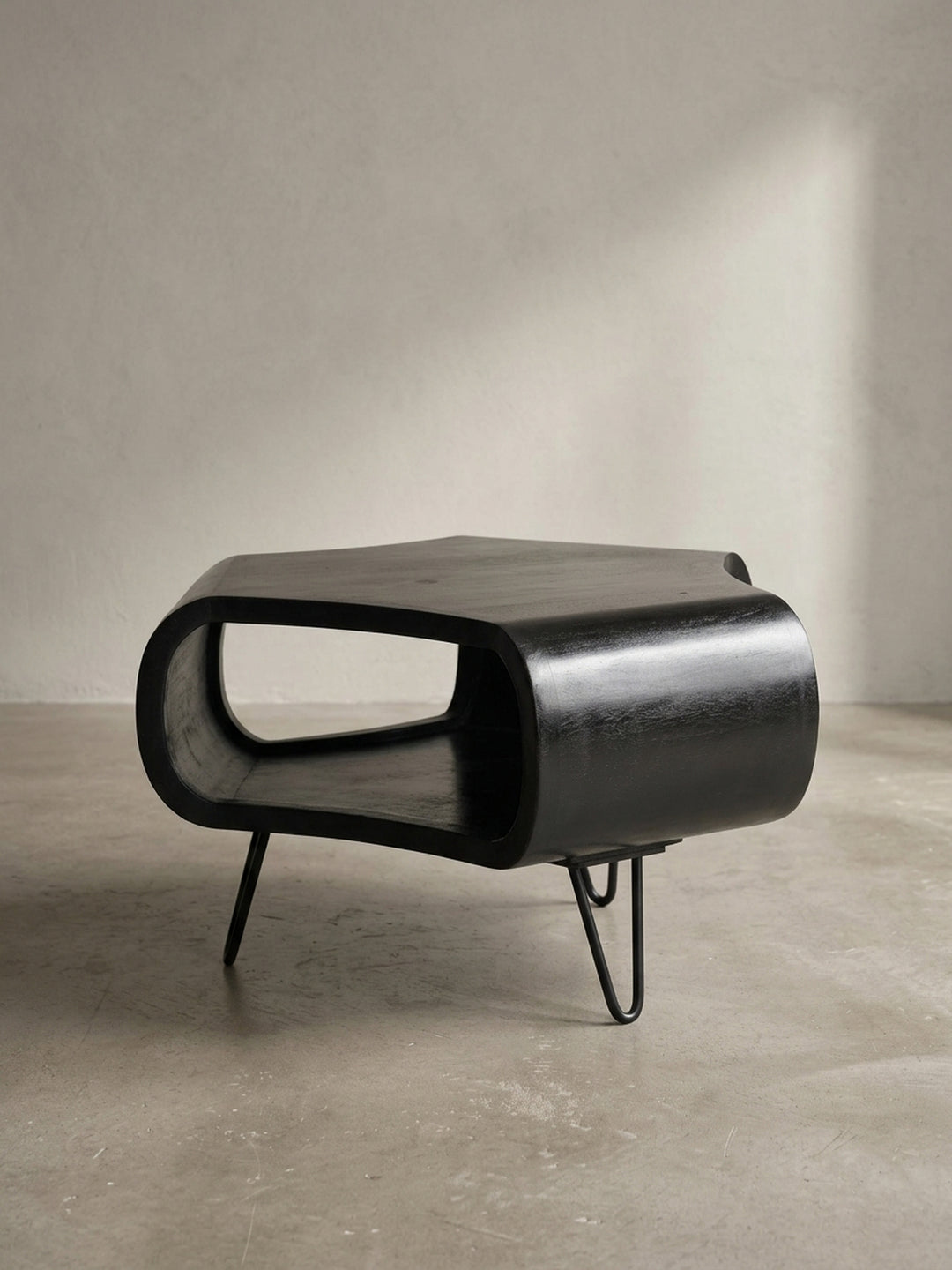 Alternative Perspektive auf den schwarzen Wohnzimmertisch, die den Kontrast zwischen dem voluminösen Holzkörper und den leichten, luftigen Beinen im Mid-Century-Stil betont._