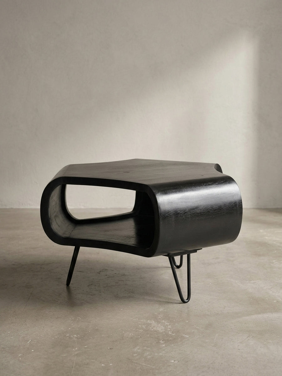 Alternative Perspektive auf den schwarzen Wohnzimmertisch, die den Kontrast zwischen dem voluminösen Holzkörper und den leichten, luftigen Beinen im Mid-Century-Stil betont._