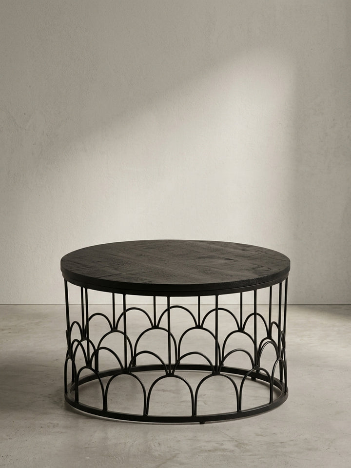 Runder Couchtisch aus schwarzem Mango Massivholz 60x60x36 cm mit dekorativem Eisengestell aus eleganten Rundbögen in Frontalansicht vor neutralem weißen Hintergrund._