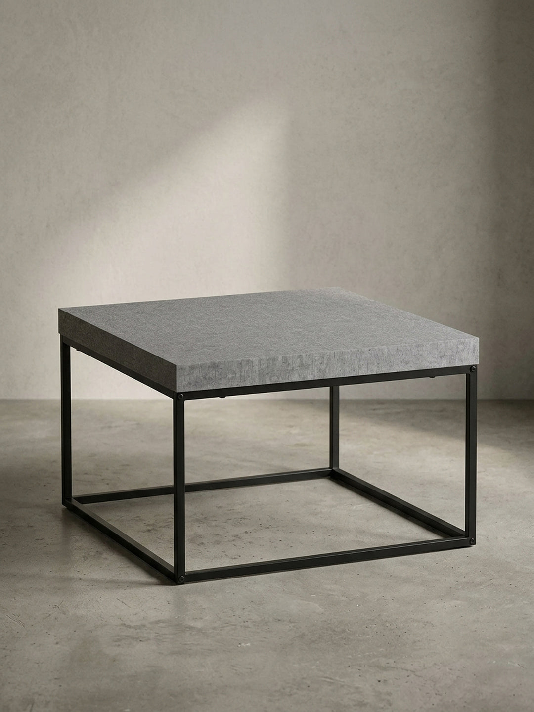 Freigestellter Couchtisch 60x60 cm in Betonoptik Grau mit minimalistischem, schwarzem Eisengestell aus einer frontalen Perspektive._