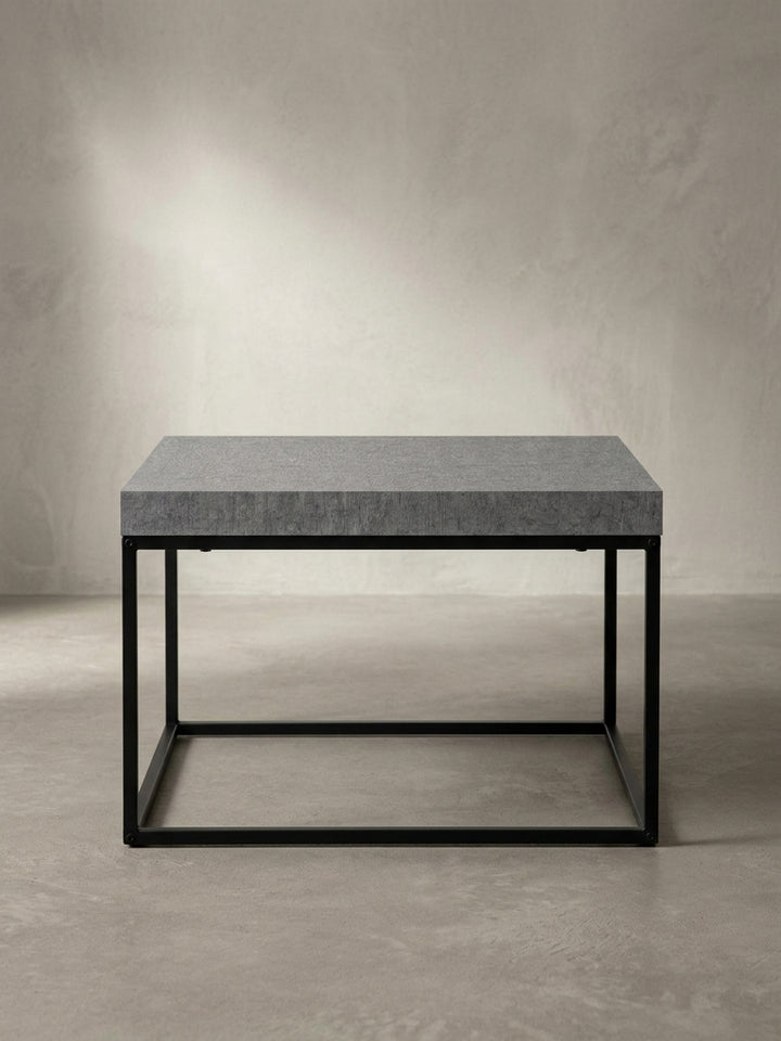 Design-Wohnzimmertisch in quadratischer Form aus der Dreiviertel-Ansicht, die das Zusammenspiel der dicken Tischplatte und des filigranen Metallgestells betont._