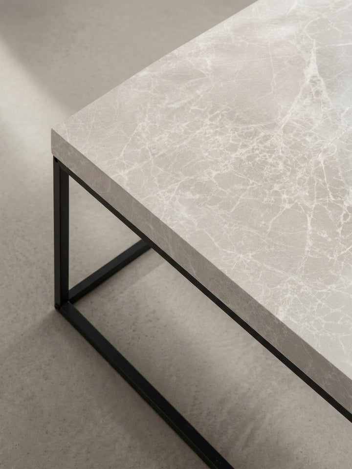 Der quadratische Couchtisch aus einer alternativen Perspektive, die das Zusammenspiel zwischen der massiven Platte und dem luftigen Metallrahmen verdeutlicht._
